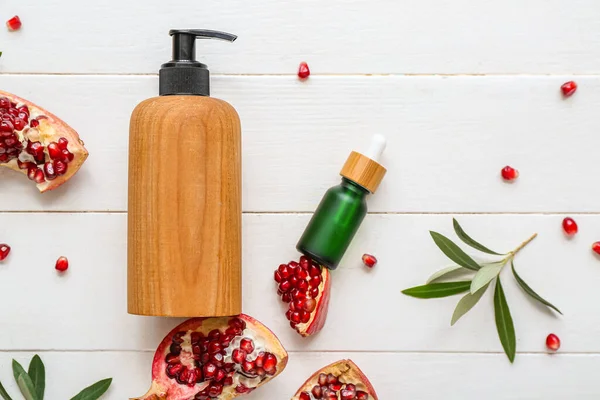 Composition with cosmetic products, pomegranate and plant branches on light wooden background