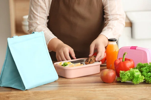 Mother packing meal in lunchbox for school on table at kitchen