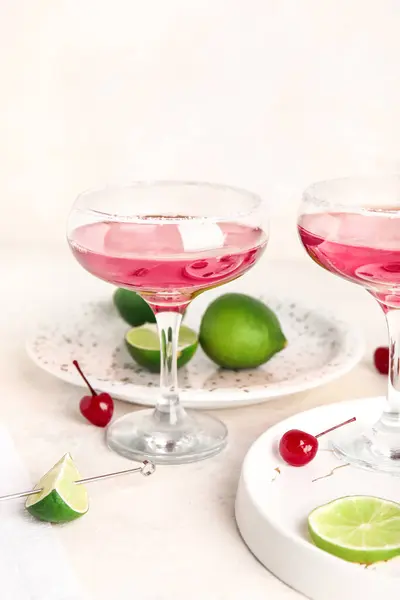 Glass of Cosmopolitan cocktail with cherries and lime on white background