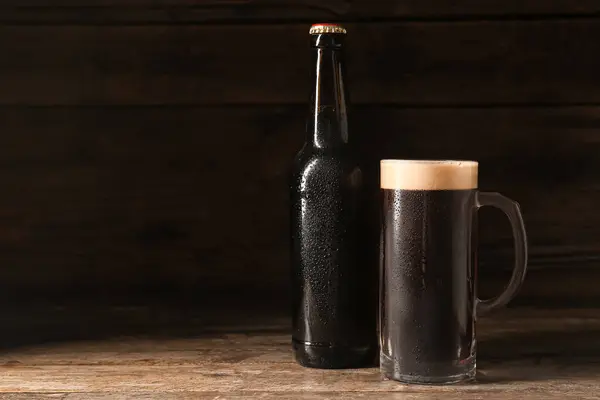 Bottle and mug of dark beer on wooden background