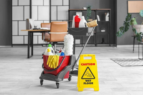 Trolley with cleaning supplies and caution sign in office