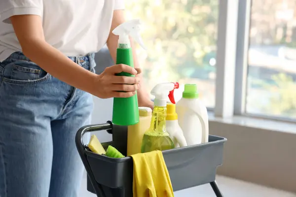 Woman with trolley of cleaning supplies in room, closeup