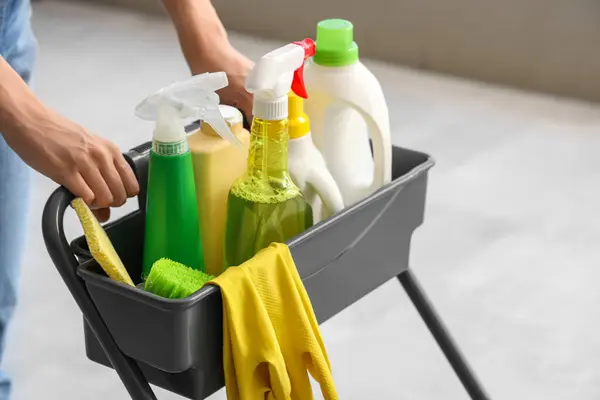 Woman with trolley of cleaning supplies in room, closeup