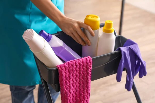 Female janitor with trolley of cleaning supplies in room, closeup