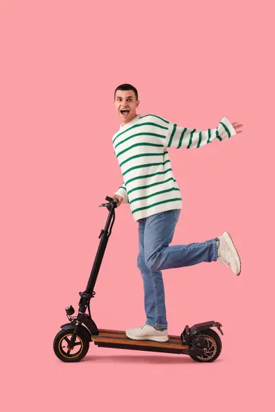 Happy young man with kick scooter on pink background
