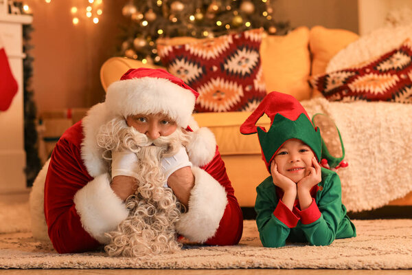 Santa Claus with cute little elf at home on Christmas eve