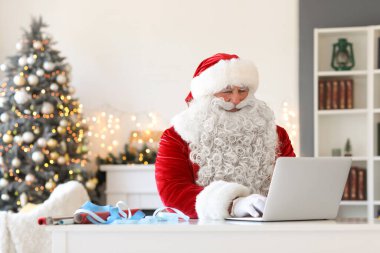 Noel Baba Noel arifesinde evde dizüstü bilgisayarla çalışıyor.
