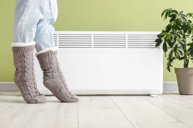 Elektrikli ısıtıcının yanında sıcak kış çorapları giymiş genç bir kadın. Isınma mevsimi kavramı