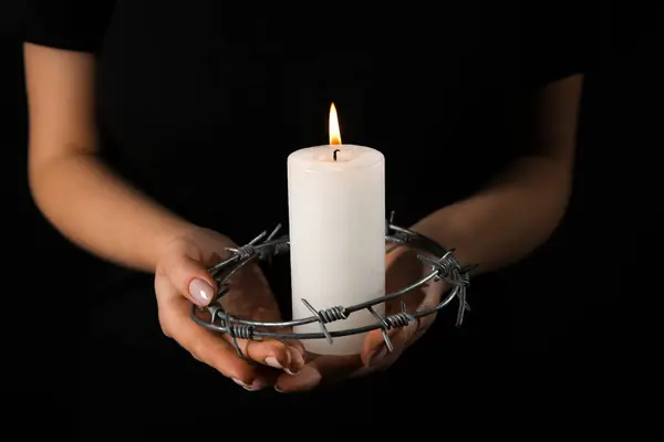 Jewish woman with burning candle and barbed wire on dark background, closeup. International Holocaust Remembrance Day