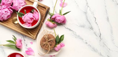 Çay fincanları, kurabiyeler ve hafif arkaplanda güzel şakayık çiçekleri olan kompozisyon.