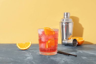 Bir bardak soğuk Negroni kokteyli, renk arka planında pipet ve titretici.
