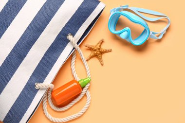 Çantalı bir şişe güneş kremi ve turuncu arka planda şnorkel maskesi.