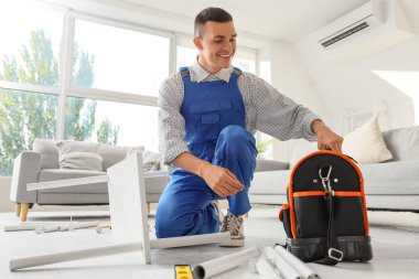 Bir çanta alet edevat taşıyan erkek işçi odada mobilya monte ediyor.