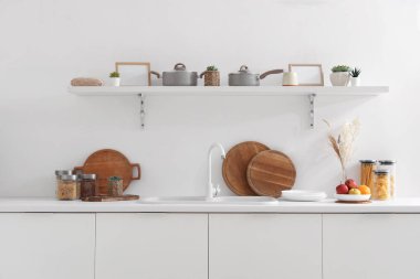 Beyaz tezgahlı, raflı, lavabolu ve çatallı modern mutfağın içi.