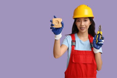Mor arka planda pense ve soketi olan genç bir elektrikçi kadın.