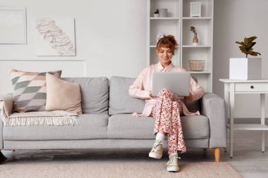 Dizüstü bilgisayarı olan genç bir kadın evdeki kanepede dinleniyor.