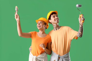 Yeşil arka planda boya fırçası ve tekerleği olan genç bir çift.