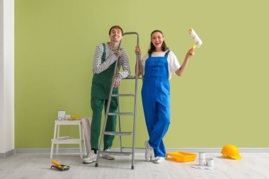 Yeşil duvarın yanında boya aletleri olan genç bir çift.