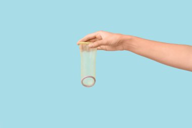 Mavi arka planda açık prezervatifli bir kadın eli. Güvenli seks konsepti