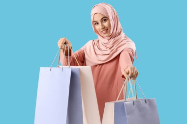 Mavi arka planda alışveriş torbaları olan güzel Müslüman kadın.