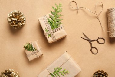 Noel hediye kutularıyla boyanmış altın kozalaklar ve bej arka planda kozalaklı dallar.