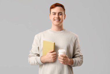 Gülümseyen adam gri arka planda kitap ve bir fincan kahve tutuyor.