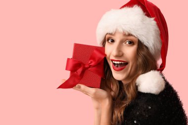 Noel Baba şapkalı, pembe arka planda hediye kutusu olan mutlu genç kadın.