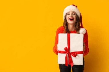 Sarı arka planda Noel Baba şapkalı genç bir kadın.