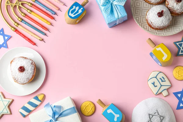 stock image Frame made of kipa, dreidels, menorah, plates with donuts and gift boxes for Hannukah celebration on pink background