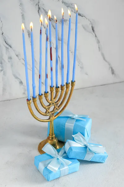 Menorah with burning candles and gifts for Hanukkah celebration on light background