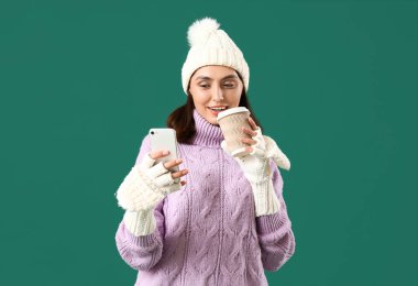 Yeşil arka planda cep telefonu kullanan, kışlık elbiseli genç bir kadın.