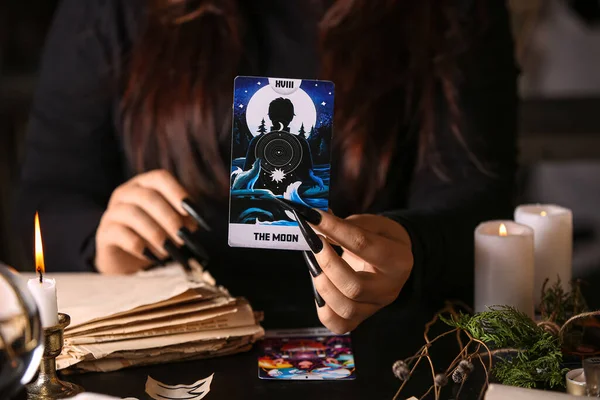 Witch with tarot card at dark table, closeup