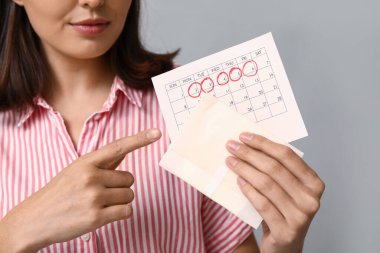 Gri arkaplanda işaretli adet günleri olan deftere ve takvime bakan güzel genç bir kadın.