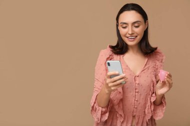 Regl fincanı ve kahverengi arka planda cep telefonu olan güzel bir genç.