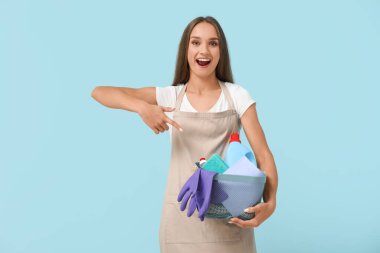 Güzel genç bayan mavi arka plandaki temizlik malzemelerine işaret ediyor.