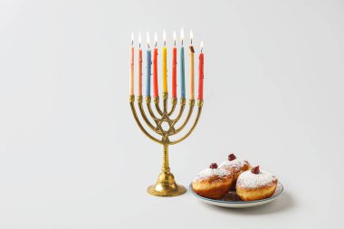 Gri arka planda Hanuka kutlaması için lezzetli çöreklerle menorah ve tabak.