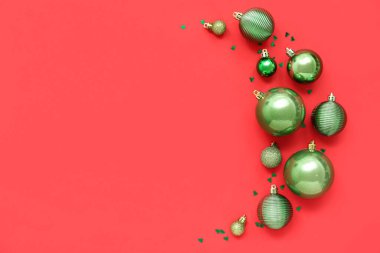 Kırmızı arka planda parıltıları olan yeşil Noel toplarıyla kompozisyon
