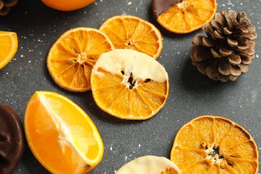 Çikolata soslu portakal dilimleri ve siyah arka planda çam kozalağı.