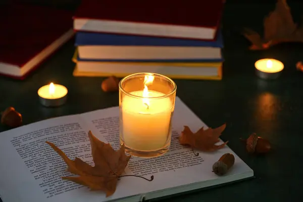 Candle, books and autumn leaves on dark background