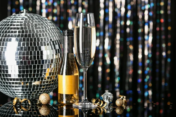 Festive New Year party composition with disco ball, bottle and glass of alcohol on blurred background.