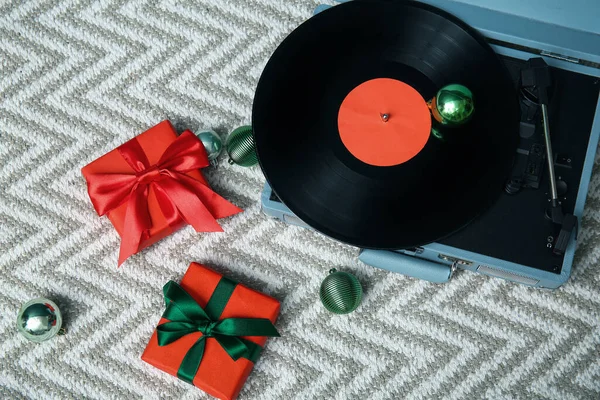 Vintage record player, Christmas gifts and balls on light rug