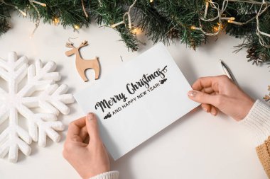 Noel kutlaması için tebrik kartı taşıyan olgun bir kadın beyaz masada, üst tarafta.