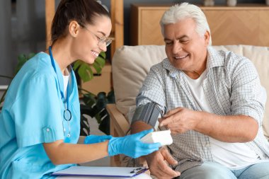 Evde yaşlı bir adamın tansiyonunu ölçen kadın hemşire.