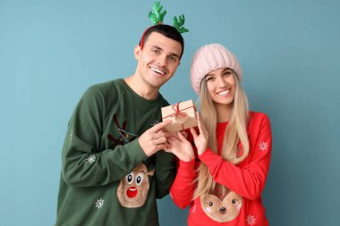 Mavi arka planda hediyeleri olan Noel kazaklı genç bir çift.