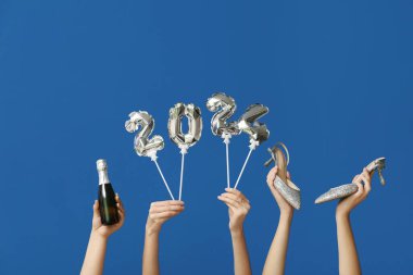 Şampanya şişesi, yüksek topuklu ayakkabılar ve mavi arka planda balonlardan yapılmış 2024 model kadın elleri.