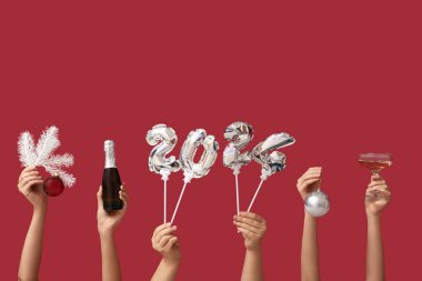 Şampanya şişesi, cam ve kırmızı arka planda balonlardan yapılmış 2024 model kadın elleri.