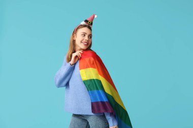 Mavi arka planda LGBT bayrağı olan Noel Baba şapkalı genç bir kadın.