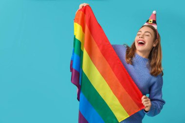 Mavi arka planda LGBT bayrağı olan Noel Baba şapkalı genç bir kadın.