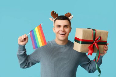 Geyik boynuzlu genç adam LGBT bayrağı ve mavi arka planda Noel hediyesi