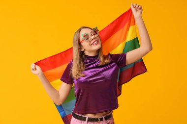 Sarı arka planda LGBT bayrağı olan Noel gözlüklü genç bir kadın.